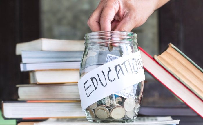 Coins and banknote in a glass jar placed on the textbook. Concept money saving for education.